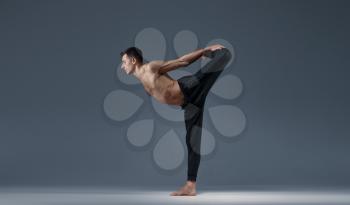 Male yoga keeps balanc in a difficult pose, grey background. Strong man doing yogi exercise, asana training, top concentration, healthy lifestyle