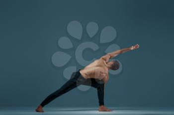 Male yoga doing stretching exercise in studio, grey background. Strong man practicing yogi , asana training, top concentration, healthy lifestyle