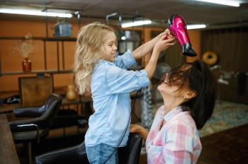 Mother and daughter using hair dryer in makeup salon. Mom and little girl play stylists together, happy childhood, glamour family