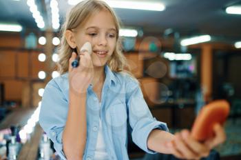 Little girl holds brush at the mirror in makeup salon. Mom and daughter play stylists together, happy childhood, glamour family, make-up