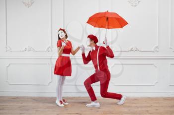 Mime artists in red costumes, scene with umbrella. Pantomime theater, parody comedian, positive emotion, humour performance, funny face mimic and grimace