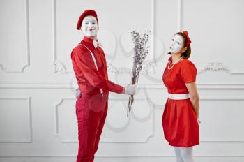 Two mime artists in red costumes, scene with the bouquet. Pantomime theater, parody comedian, positive emotion, humour performance, funny face mimic and grimace