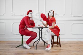 Two mime artists in red costumes, scene at the table. Pantomime theater, parody comedian, positive emotion, humour performance, funny face mimic and grimace