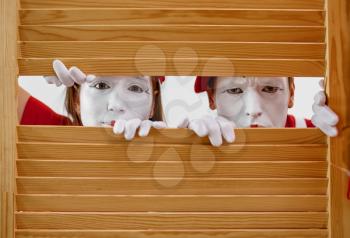 Two mime artists with makeup look through wooden partition. Pantomime theater, parody comedian, positive emotion, humour performance, funny face mimic and grimace