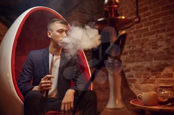 Young man smokes in hookah bar, hooka chill out. Shisha smoking, traditional bong culture, tobacco aroma for relaxation, rest with hooka