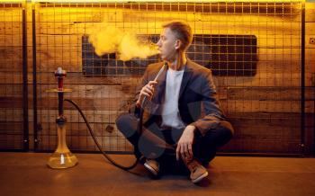 Young man smokes on the floor, hookah bar, hooka chill out. Shisha smoking, traditional bong culture, tobacco aroma for relaxation, rest with hooka