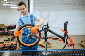 Bicycle factory, worker at assembly line, wheel installation. Male mechanic in uniform installs cycle parts in workshop