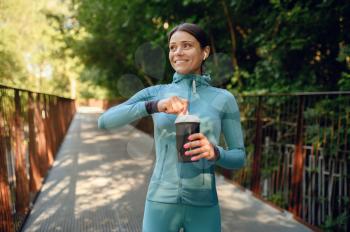 Morning training in park, woman in headphones drinks water on walkway. Female runner goes in for sports at sunny day, healthy lifestyle, jogger on outdoors workout