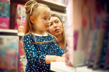 Mother and pretty little girl choosing a doll in toy store. Mom and adorable daughter near the showcase in toyshop, happy childhood, family makes a purchase in shop