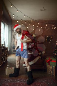 Bad Santa claus gangster with gift bag and gun, nasty party, humor. Unhealthy lifestyle, bearded man in holiday costume, new year and alcoholism