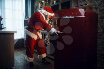 Bad impudent Santa claus opens the refrigerator, nasty party, humor. Unhealthy lifestyle, bearded man in holiday costume, new year and alcoholism