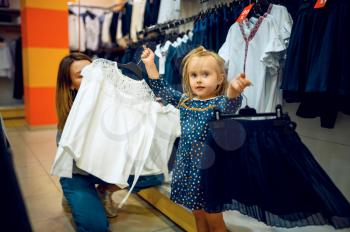 Mother and little baby choosing skirt in kid's store. Mom and adorable girl near the showcase in children's shop, happy childhood, family makes a purchase in kid's market