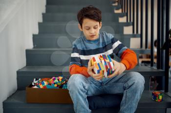 Little boy sitting on the steps and play with puzzle cubes. Toy for brain and logical mind training, creative game, solving of complex problems