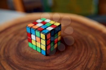 Classical colorful puzzle cube on wooden stump, closeup view, nobody. Toy for brain and logical mind training, creative game, solving of complex problems