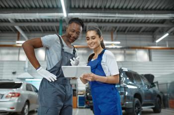 Male and female mechanics inspects engine, car service. Vehicle repairing garage, men in uniform, automobile station interior on background. Professional auto diagnostics