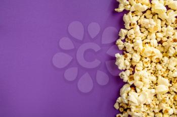 Popcorn border isolated on purple background, top view. Pop corn texture, tasty wallpaper design, movie or cinema food concept