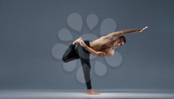 Male yoga keeps balanc in a difficult pose on one leg, grey background. Strong man doing yogi exercise, asana training, top concentration, healthy lifestyle
