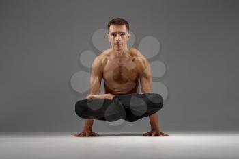 Male yoga keeps balanc on hands in classical pose, meditation position, grey background. Strong man doing yogi exercise, asana training, top concentration, healthy lifestyle