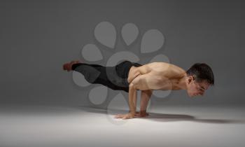 Male yoga keeps horizontal balanc on hands, meditation position, grey background. Strong man doing yogi exercise, asana training, top concentration, healthy lifestyle