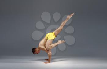 Muscular yoga stands on hands in difficult pose, meditation position, grey background. Strong man doing yogi exercise, asana training, top concentration, healthy lifestyle