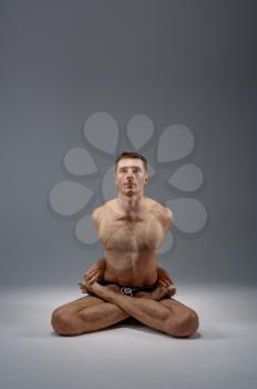 Yoga sits in classical pose, meditation position, perfect stretching, grey background. Strong man doing yogi exercise, asana training, top concentration, healthy lifestyle