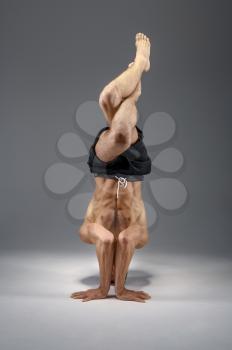 Male yoga standing on his head and hands, meditation, grey background. Strong man doing yogi exercise, top concentration
