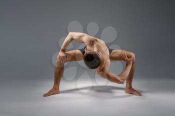 Male yoga stands in a difficult pose, perfect stretching, meditation, grey background. Strong man doing yogi exercise, asana training, top concentration, healthy lifestyle