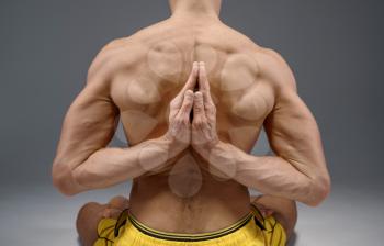 Yoga sits in classical pose with hands behind his back, meditation position, perfect stretching, grey background. Strong man doing yogi exercise, top concentration, healthy lifestyle