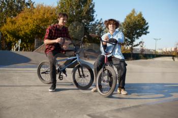 Two bmx bikers poses on ramp in skatepark. Extreme bicycle sport, dangerous cycle exercise, street riding, biking in summer park