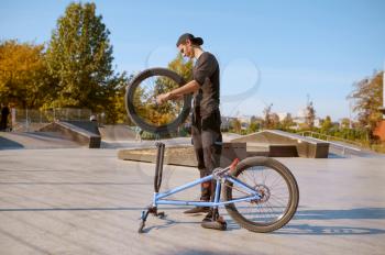 Young male bmx biker adjusts his bike,teenager on training in skatepark. Extreme bicycle sport, dangerous cycle exercise, risk street riding, biking in summer park