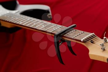 Electric guitar fretboard with capodaster, closeup, red background, nobody. String musical instrument, electro sound, electronic music, equipment for stage concert