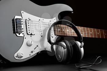 Electric guitar and headphones on black background, nobody. String musical instrument, electro sound, electronic music, equipment for stage concert