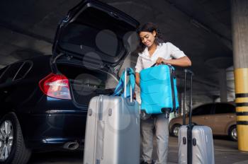 Happy woman with many suitcases in car parking. Female traveler with luggage in vehicle park lot, passenger with bag. Girl with baggage near automobile