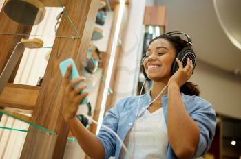 Woman listening to music in headphones store. Female person in audio shop, showcase with earphones on background, buyer in multimedia salon