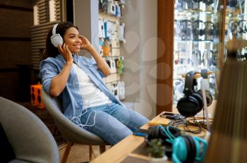 Customer trying on headphones in audio store, music fan. Female person in music shop, showcase with earphones on background, buyer in multimedia salon