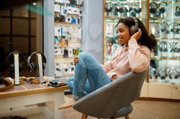 Buyer trying on headphones in audio store, music fan. Female person in music shop, showcase with earphones on background, woman in multimedia salon