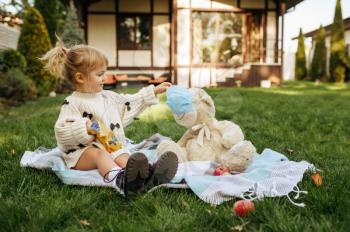 Kid play with teddy bear in the garden. Child with soft toy sitting on the lawn on backyard. Little girl having fun on playground outdoors, happy childhood