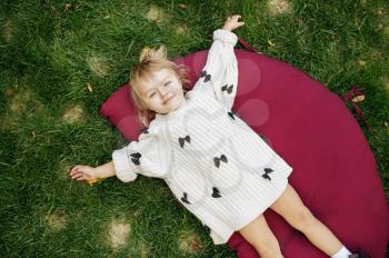 Little girl lying on the grass in the garden. Female child poses on the lawn on backyard. Kid having fun on playground outdoors, happy childhood