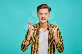 Focused man with crossed fingers, blue background, emotion. Face expression, male person looking on camera in studio, emotional concept, feelings