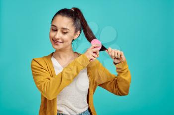 Pretty woman combs her hair, blue background, positive emotion. Face expression, female person looking on camera in studio, emotional concept, feelings