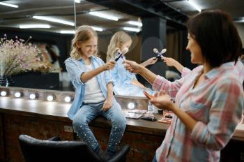 Mother and daughter in salon, makeup artists. Mom and little girl play stylists together, happy childhood, glamour family