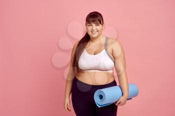 Smiling overweight woman with fitness mat, pink background, body positive. Obesity fighting, striving for a healthy lifestyle