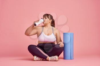 Overweight sportive woman drinks water, body positive, pink background. Obesity fighting, striving for a healthy lifestyle