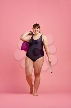Overweight woman in swimsuit holds fins and mask, body positive, pink background. Obesity fighting, cheerful female person without complexes, striving for a healthy lifestyle