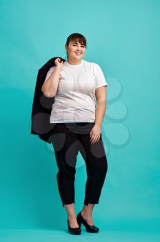 Overweight woman in suit poses in studio, body positive, blue background. Obesity fighting, cheerful female person without complexes