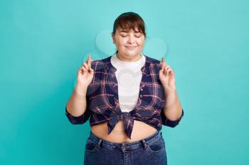 Pretty overweight woman makes a wish, body positive, blue background. Obesity fighting, cheerful female person without complexes