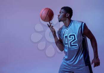 Basketball player with ball shows his skill in studio, neon background. Professional male baller in sportswear playing sport game, tall sportsman