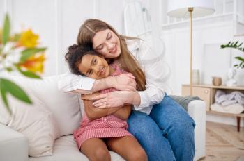 Happy mother hugs her little daughter on sofa in living room.Mom and female child leisures in their house together, good relationship, parental care