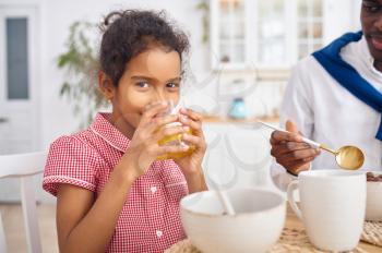 Happy father and little daughter drinks juice on breakfast. Smiling family eats on the kitchen in the morning. Dad feeds female child, good relationship