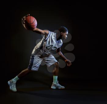 Basketball player with ball, practicing in action in studio, black background. Professional male baller in sportswear playing sport game, sportsman